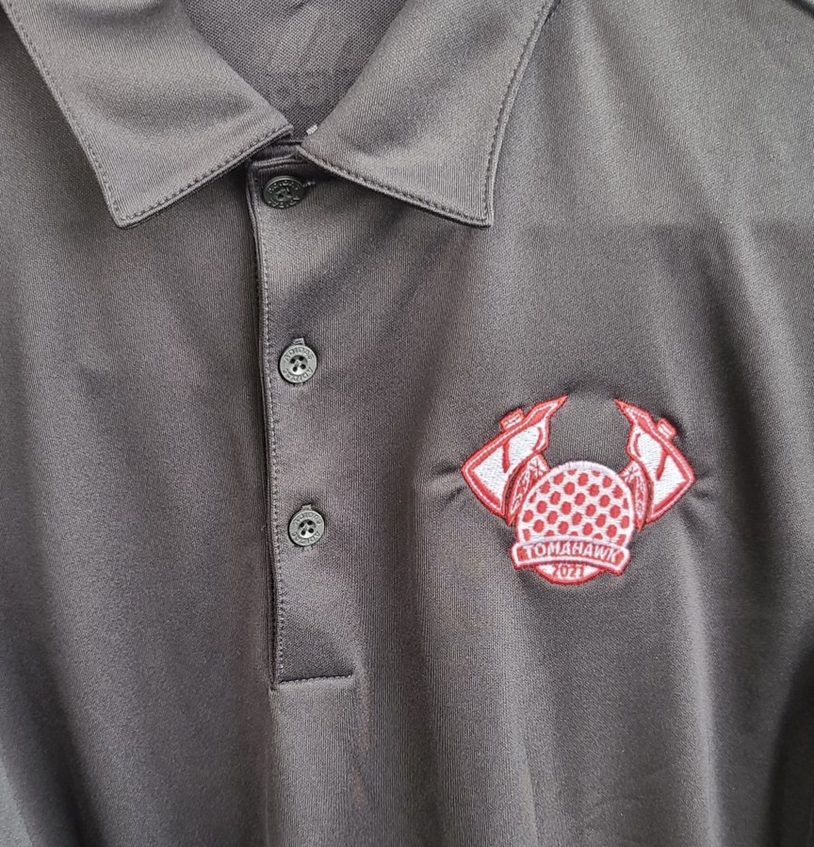 The Team Tomahawk badge embroidered on the left chest of a charcoal polo shirt